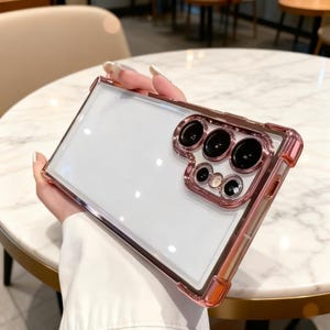 May include: Clear phone case with a rose gold frame and camera lens protector. The case has a transparent back, showcasing the phone's design. The rose gold accents provide a stylish contrast.