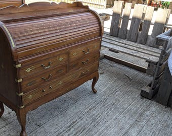 May include: A vintage wooden roll-top desk with a warm brown finish. The desk features multiple drawers with brass hardware and curved legs. The roll-top is made of wooden slats. The desk is approximately 40 inches wide.