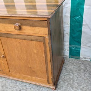 May include: A wooden sideboard featuring a light brown finish with darker brown wood accents. The piece includes two top drawers with round wooden knobs and two lower cabinet doors with matching round knobs. The top surface has a smooth, polished finish.