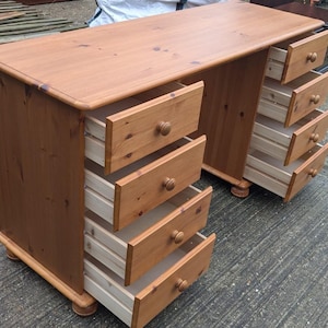 May include: A light brown wooden desk with multiple drawers. The desk has a rectangular top and two sets of drawers on either side. Each set has five drawers with round wooden knobs. The drawers are open, revealing the interior.