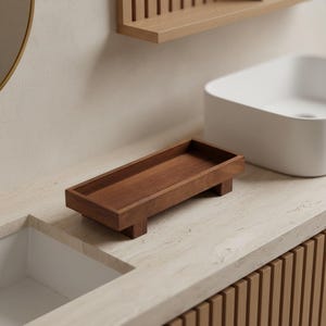 May include: A rectangular wooden tray with a smooth, dark brown finish and a visible wood grain. The tray features four short, block-style feet at the corners, elevating the base slightly above the surface. It has a simple, open-top design.