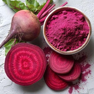 May include: Overhead shot of fresh beets and beet powder. A whole beet with leaves and a sliced beet revealing concentric rings are next to a small bowl filled with vibrant pink beet powder. Sliced beets are fanned out.