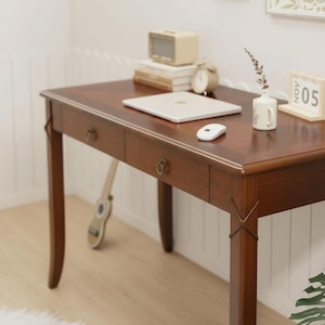 May include: A dark brown wooden desk with two drawers, a laptop, and a small radio. A white mouse, a small vase with a sprig, and a calendar are on the desk. A guitar leans against the desk.