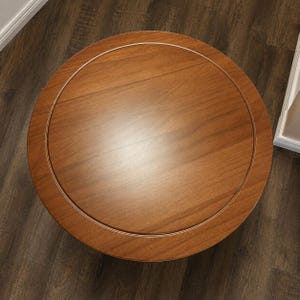Peut inclure: Une table ronde en bois avec une finition brun moyen lisse. Le plateau pr&eacute;sente un d&eacute;tail d'incrustation circulaire qui cr&eacute;e une bordure subtile autour du centre. Le grain du bois est visible sur toute la surface, montrant des motifs naturels.