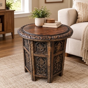 May include: A round wooden side table with a dark brown finish, featuring intricate floral carvings along the circular tabletop edge and vertical panels. The table has a sturdy base with carved details and a smooth, flat top surface.