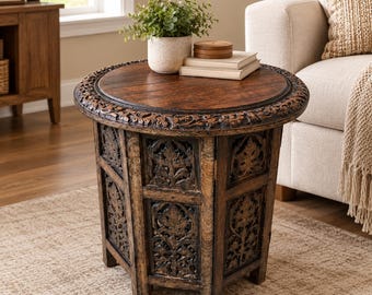 May include: A round wooden side table with a dark brown finish, featuring intricate floral carvings along the circular tabletop edge and vertical panels. The table has a sturdy base with carved details and a smooth, flat top surface.