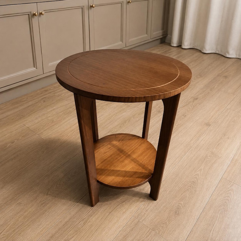 Peut inclure: Une table d'appoint ronde en bois dot&eacute;e d'un plateau circulaire lisse avec un d&eacute;tail de bordure incrust&eacute; subtil. La table est soutenue par quatre pieds incurv&eacute;s qui s'&eacute;tendent vers le bas, reliant une &eacute;tag&egrave;re inf&eacute;rieure circulaire plus petite.
