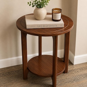 Peut inclure: Une table d'appoint ronde en bois avec une finition brun fonc&eacute;, dot&eacute;e de quatre pieds droits et d'une &eacute;tag&egrave;re circulaire inf&eacute;rieure. Sur le plateau se trouvent un livre beige intitul&eacute; LIVE BEAUTIFULLY, un petit vase en c&eacute;ramique cr&egrave;me et une bougie.