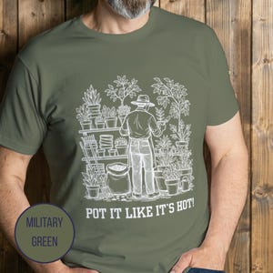 May include: Military green t-shirt with a white graphic of a gardener tending plants. The graphic includes the text "POT IT LIKE IT'S HOT!" and a circular label that says "MILITARY GREEN".