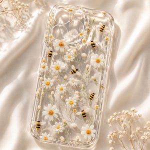 Puede incluir: Funda transparente para teléfono decorada con margaritas blancas con centros amarillos y pequeñas abejas negras y amarillas. La funda es transparente, lo que permite que se vea el color del teléfono. El diseño está sobre un fondo blanco suave.
