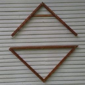 May include: Two wooden triangular shelves, one inverted, are mounted on a light grey, horizontally-panelled wall. The shelves are a warm brown colour and appear to be made of bamboo or a similar material. The shelves are empty.