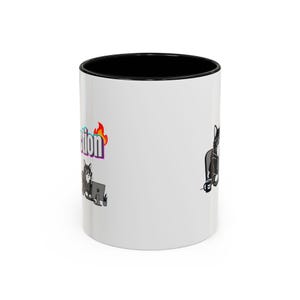 May include: White ceramic coffee mug with a black interior. The mug features a cartoon cat design with the word "Action" in a colorful, flame-like font. The cat is depicted working on a computer.