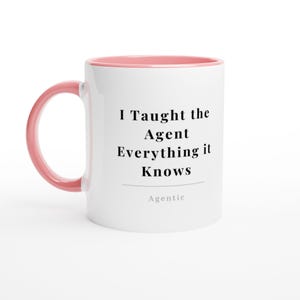 May include: A white ceramic mug with a pink handle and interior rim. The front features the black text 'I Taught the Agent Everything it Knows' followed by a horizontal line and the word 'Agentic' in a smaller, lighter grey font.