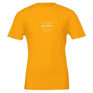 May include: A bright yellow short-sleeve t-shirt featuring white text centred on the chest. The text reads "Trigger HAPPY" in a bold, serif font, with the words "cloud life" printed in a smaller, thinner font below a horizontal line.