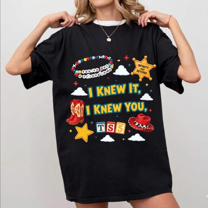 Może przedstawiać: Czarny t-shirt z kolorowym nadrukiem graficznym z tekstem "I KNEW IT, I KNEW YOU", "TS5", "You've got a friend in me" oraz "INFINITY AND BEYOND". Wz&oacute;r zawiera ilustracje czerwonych kowbojek, czerwonego kapelusza, gwiazd i chmur.