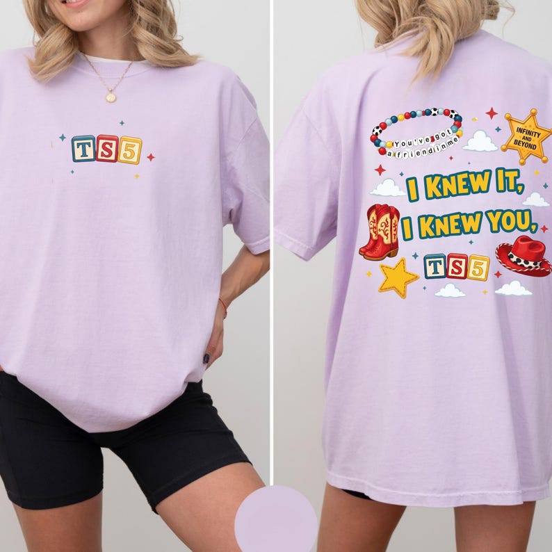 May include: A light purple t-shirt featuring a small graphic on the front with the text TS5 in colorful blocks. The back displays a beaded bracelet, a gold star, red cowboy boots, a red hat, and the text I KNEW IT, I KNEW YOU, TS5.