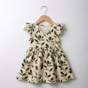 May include: A sleeveless dress in a light cream color featuring a dark green leaf pattern. The dress has a V-neckline, ruffled cap sleeves, and a gathered waistline that flows into a flared skirt. It is displayed on a wooden hanger.