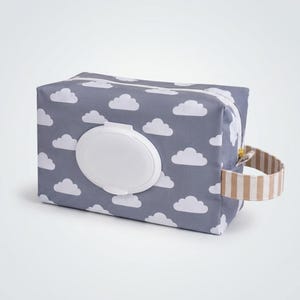 May include: A rectangular gray wipe case featuring a repeating white cloud pattern. The case includes a centered white plastic flip-top lid for dispensing and a side handle made of beige and white striped fabric with a gold-toned zipper pull.