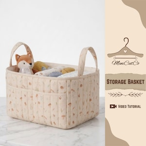 May include: A beige quilted storage basket with two handles and side pockets, filled with baby items. The basket features a delicate floral pattern in brown and green. A stuffed fox toy is visible inside. The text "STORAGE BASKET" is on the side.