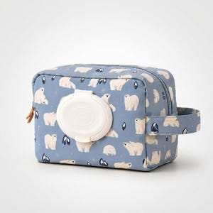 May include: A rectangular blue pouch featuring a repeating pattern of white polar bears and small dark blue shapes. The pouch has a white plastic flip-top lid centered on the front panel, a zippered closure, and a fabric handle on the right side.
