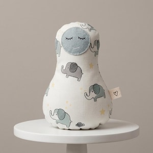 May include: A pear-shaped plush toy featuring a white fabric base with a repeating pattern of grey and light blue elephants and small yellow stars. The top section has a circular light blue felt face with embroidered closed eyes and a smile.