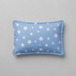 May include: A rectangular throw pillow featuring a light blue fabric base with a repeating pattern of white five-pointed stars. The pillow has stitched edges and a soft, stuffed appearance, providing a consistent look across the entire surface.