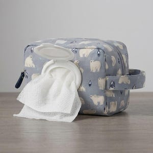 Könnte beinhalten: Ein rechteckiges Feuchttuch-Etui aus hellgrauem Stoff mit einem wiederkehrenden Muster aus weißen Eisbären. Das Etui verfügt über einen weißen Kunststoff-Klappdeckel auf der Vorderseite, durch dessen Öffnung ein weißes, strukturiertes Tuch ragt.