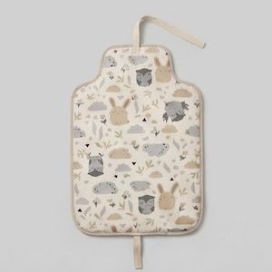 May include: A portable changing mat featuring a cream-coloured background with a repeating pattern of beige rabbits, grey owls, and soft grey clouds. The rectangular mat has rounded corners and a fabric strap attached to the top and bottom edges.
