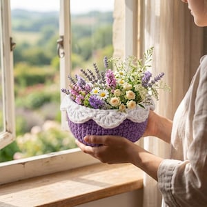May include: A crocheted purple basket filled with a variety of fresh flowers, including lavender, daisies, and small white roses. The basket has a white scalloped trim. The scene is set near an open window with a view of a green landscape.