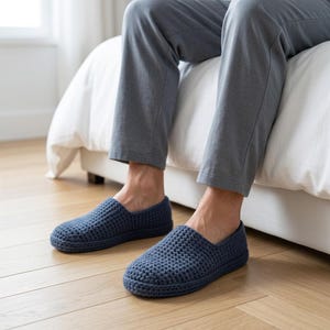 May include: A pair of dark blue slip-on slippers featuring a textured, crocheted knit construction with a rounded toe and a low-profile design. The slippers are crafted from a thick yarn material and provide full coverage for the top of the foot.