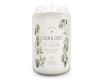 May include: A lit, clear glass candle jar with a white label that reads "CALM & COZY". The label is decorated with green eucalyptus leaves. The candle is 13.75 oz (390 g) and made with natural soy wax.