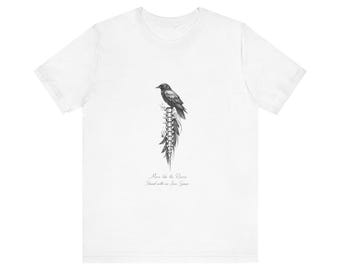May include: White t-shirt featuring a detailed black and white illustration of a raven perched on a spine-like structure. The text "Move like the Raven, Stand with me Iron Spine" is printed below the graphic.