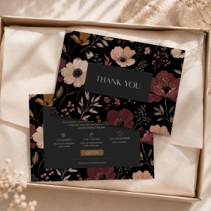 Puede incluir: Dos tarjetas florales de agradecimiento con fondo negro y variedad de flores en tonos rojos, crema y amarillos. Las tarjetas tienen el texto "THANK YOU" y otros textos. Las tarjetas están dentro de una caja marrón.