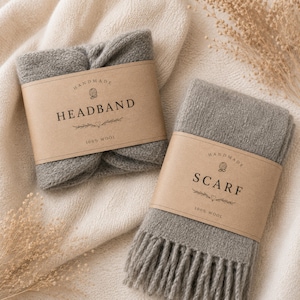 Puede incluir: Dos accesorios de lana gris: una diadema y una bufanda. La diadema está doblada y envuelta con una etiqueta de papel marrón que dice "HEADBAND" y "100% WOOL". La bufanda tiene flecos y una etiqueta que dice "SCARF" y "100% WOOL".