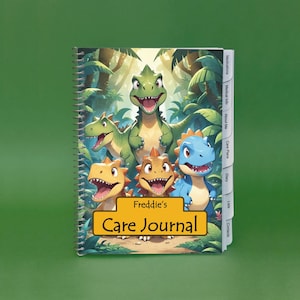 May include: A spiral-bound care journal featuring a colorful illustration of cartoon dinosaurs. The cover displays the text "Freddie's Care Journal" in a gold-colored banner. The journal has tabbed sections for medications, medical info, and more.