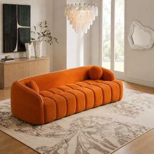 May include: A vibrant orange sofa featuring a channel-tufted design with rounded edges and a white piped trim. The sofa includes two matching cylindrical bolster pillows positioned at each end of the seat, providing a structured and uniform appearance.