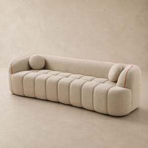 May include: A beige sofa with a channel-tufted seat and backrest, featuring rounded armrests and a thin orange piping detail along the top edges. The piece includes two small, round, matching beige accent cushions placed at each end.