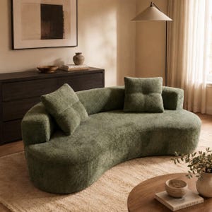 May include: A curved sofa upholstered in sage green textured fabric, featuring a low backrest and two matching square throw pillows. The sofa has a rounded, continuous silhouette with a deep seat and a soft, fuzzy surface texture throughout.