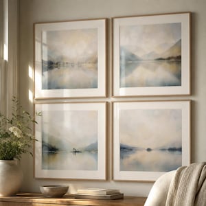 May include: A set of four square wall art prints in light wood frames, each depicting a serene landscape of mountains and water in soft, muted tones of blue, gray, and beige, featuring hazy reflections on the water surface and distant hills.