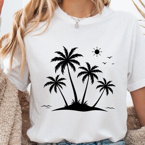 May include: A white short-sleeved t-shirt featuring a black graphic print of four palm trees on a small island. The design includes a small sun and three birds flying in the sky above the trees, with simple wavy lines representing water.