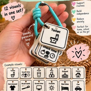 May include: A set of 12 white square plastic visual communication cards with black icons and text, including labels like Toilet, Snack time, Drink, Play, School, Home, Get dressed, Brush teeth, Screen time, Outside, Bed time, and Car, on a blue paracord loop.