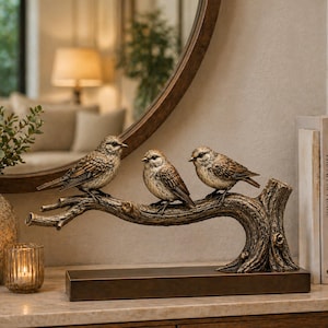 May include: A decorative sculpture of three detailed bird figurines perched on a bronze-coloured branch. The birds have brown and tan feathers. The sculpture sits on a rectangular base, suitable for home decor.