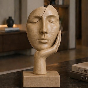 Può includere: Scultura beige di un volto sereno con gli occhi chiusi, appoggiato su una mano. La scultura è montata su una base rettangolare. Il volto è diviso a metà. Oggetto decorativo.