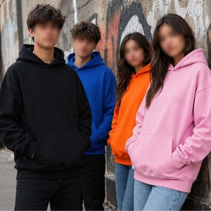 Peut inclure: Quatre personnes portant des sweats à capuche de couleurs unies : noir, bleu, orange et rose. Chaque sweat à capuche a une poche avant et une capuche. Ils se tiennent devant un mur couvert de graffitis, portant des jeans bleus.