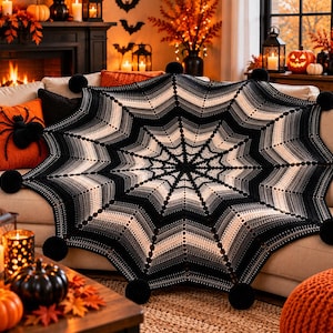 May include: A large, circular crochet blanket featuring a spiderweb pattern in a gradient of black, charcoal, and white yarn. The edges of the blanket are scalloped and finished with several large, round, black pom-poms attached at each point.