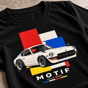 Peut inclure: Un t-shirt noir avec un graphisme représentant une voiture de sport vintage blanche orientée vers la droite. Derrière la voiture se trouvent des formes rectangulaires rouges, blanches et bleues. Le texte MOTIF since 2026 est inscrit en blanc.