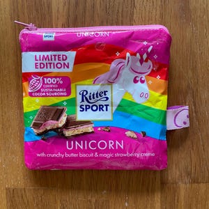 Könnte beinhalten: Ein pinkfarbener Reißverschlussbeutel mit Regenbogenmuster und einer Einhorn-Illustration. Der Beutel trägt den Text "UNICORN" und "LIMITED EDITION" mit dem Ritter Sport Logo und Text über Kakao und Erdbeercreme.