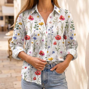 May include: A long-sleeved button-down shirt in white, featuring a botanical print of red poppies, yellow wildflowers, and blue cornflowers. The shirt has a classic collar, a front button placket, and cuffs that are rolled up to the mid-forearm.