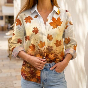 May include: A long-sleeve button-down shirt featuring a gradient print of autumn maple leaves in shades of orange, yellow, and brown. The shirt has a classic collar, a front button placket, and cuffs that are rolled up to the mid-forearm.