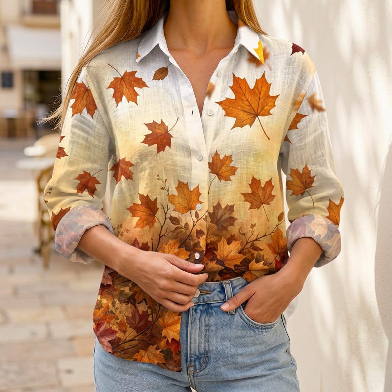 May include: A long-sleeve button-down shirt featuring a gradient print of autumn maple leaves in shades of orange, yellow, and brown. The shirt has a classic collar, a front button placket, and cuffs that are rolled up to the mid-forearm.